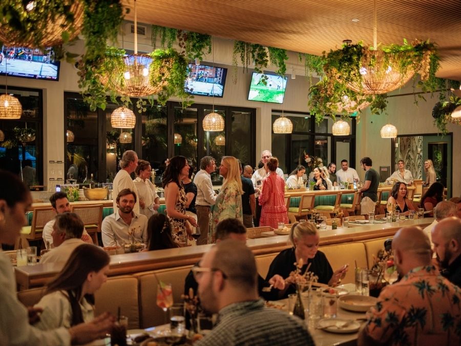 Guests dining and socializing inside Florida Room restaurant with warm lighting and greenery