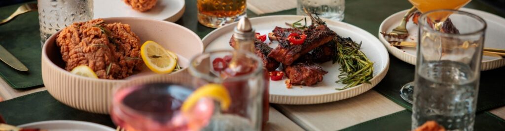 Table spread with fried chicken, ribs, cocktails, and sides at Florida Room